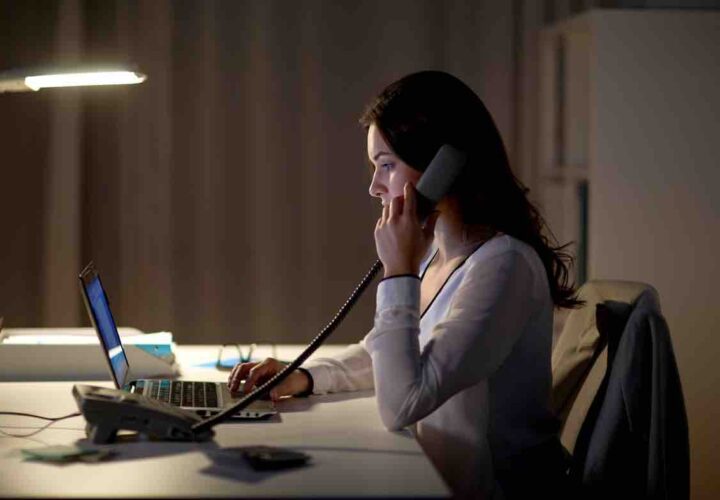 woman with laptop calling on phone at night office